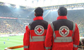 Foto: Zwei Sanitäter stehen in einemFußballstadion und schauen auf das Feld.